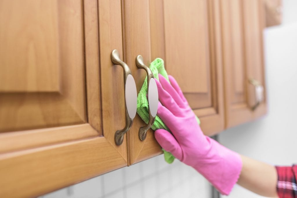 Someone cleaning grease off of kitchen cabinets whiel wearing a pink rubber glove.