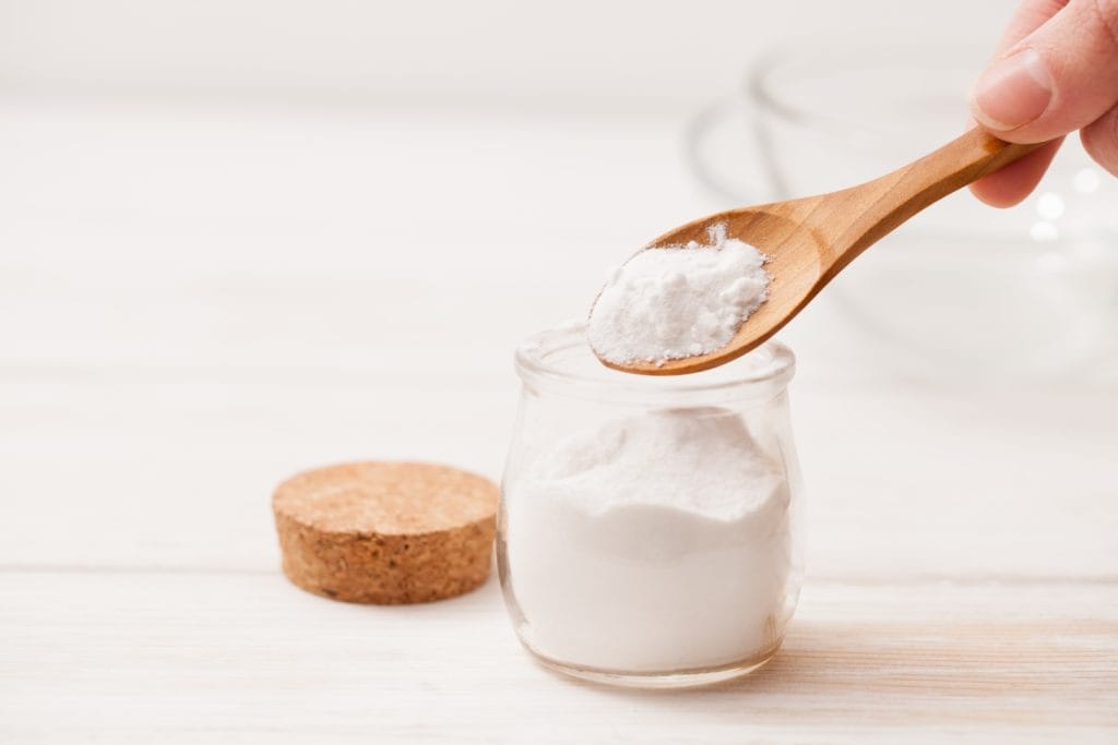 Someone scooping baking soda out of a glass jar with a wooden spoon. Baking soda is a great way to clean grease off of kitchen cabinets.