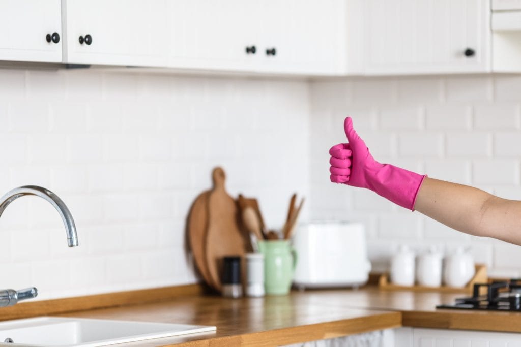 Someone in a clean kitchen giving a thumbs up while wearing a pink rubber cleaning glove.