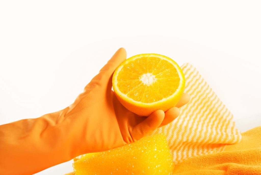 Someone in an orange cleaning glove holding an orange cut in half.
