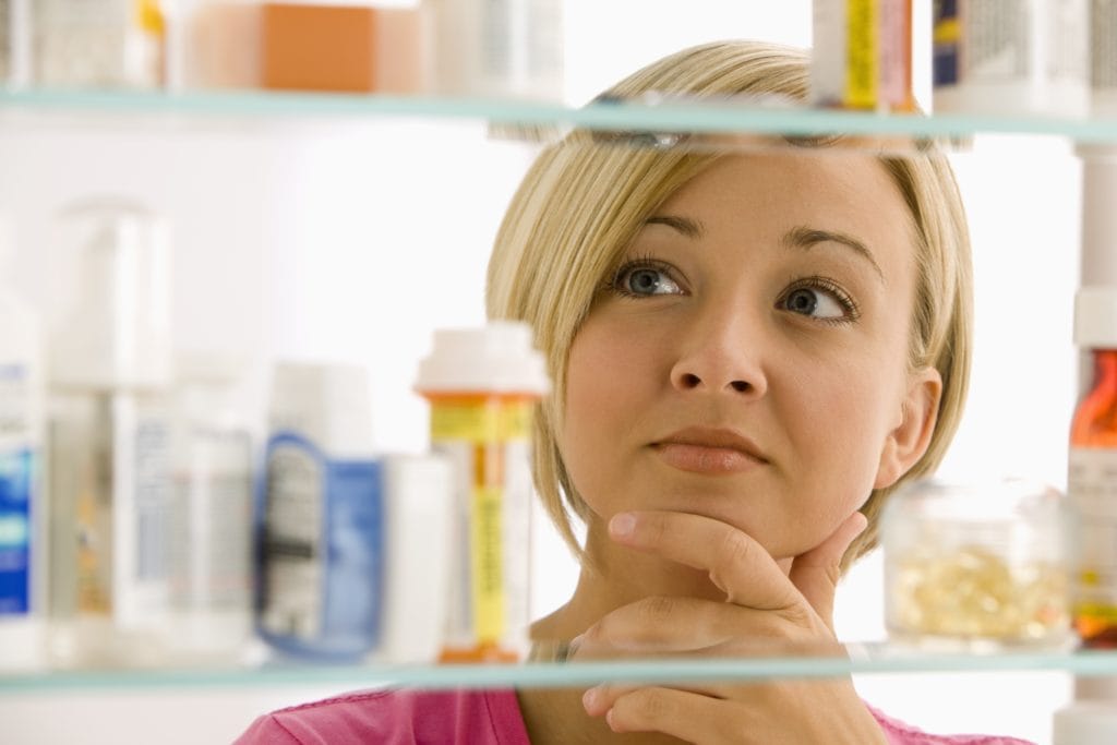 A young woman is looking through her medicine cabinet.