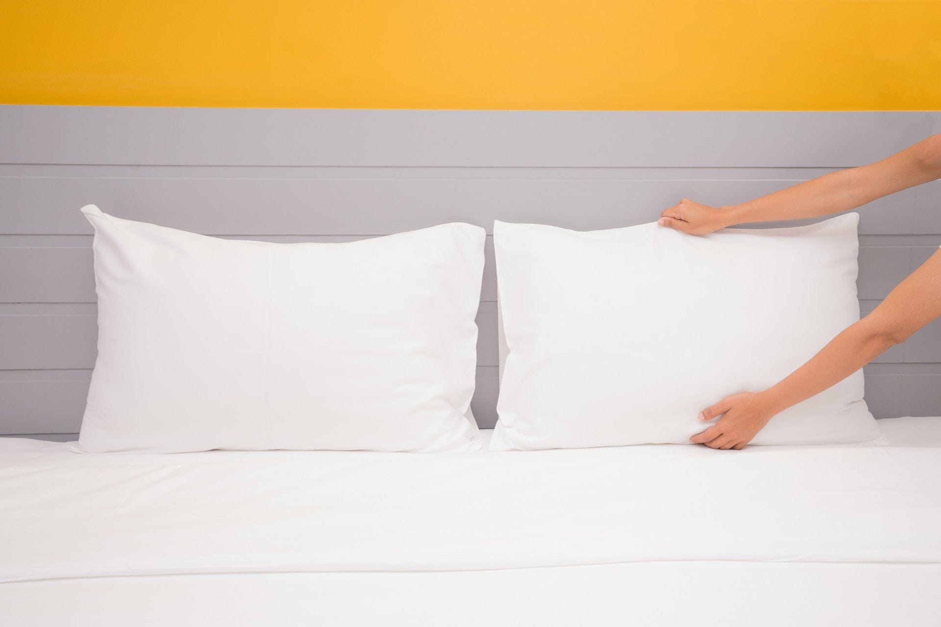 woman fixing white pillows on a bed