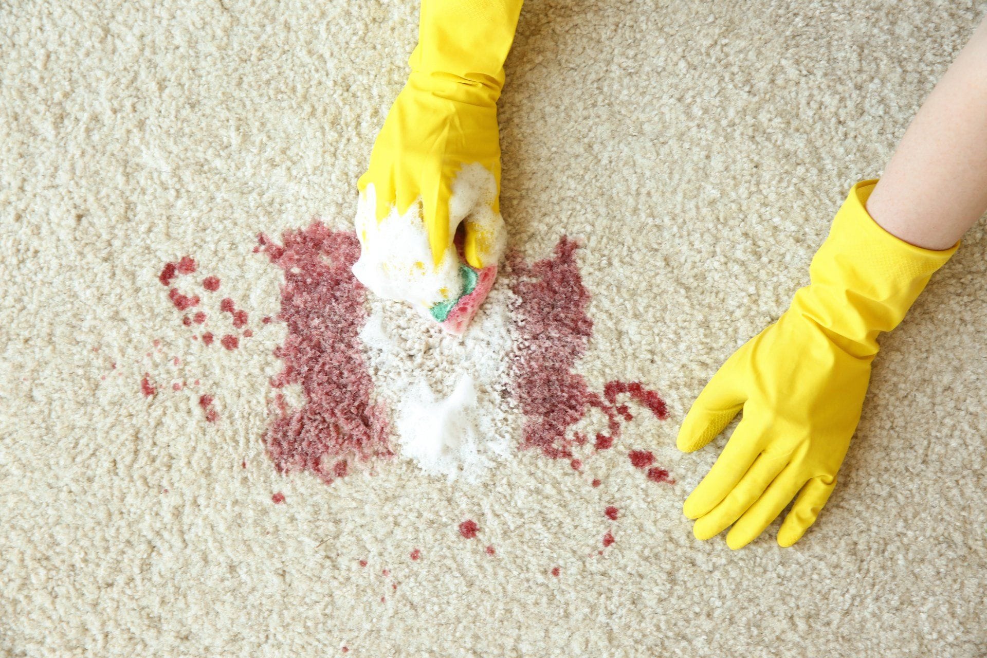 a person yellow rubber gloves cleaning a red wine stain from carpet with a sponge