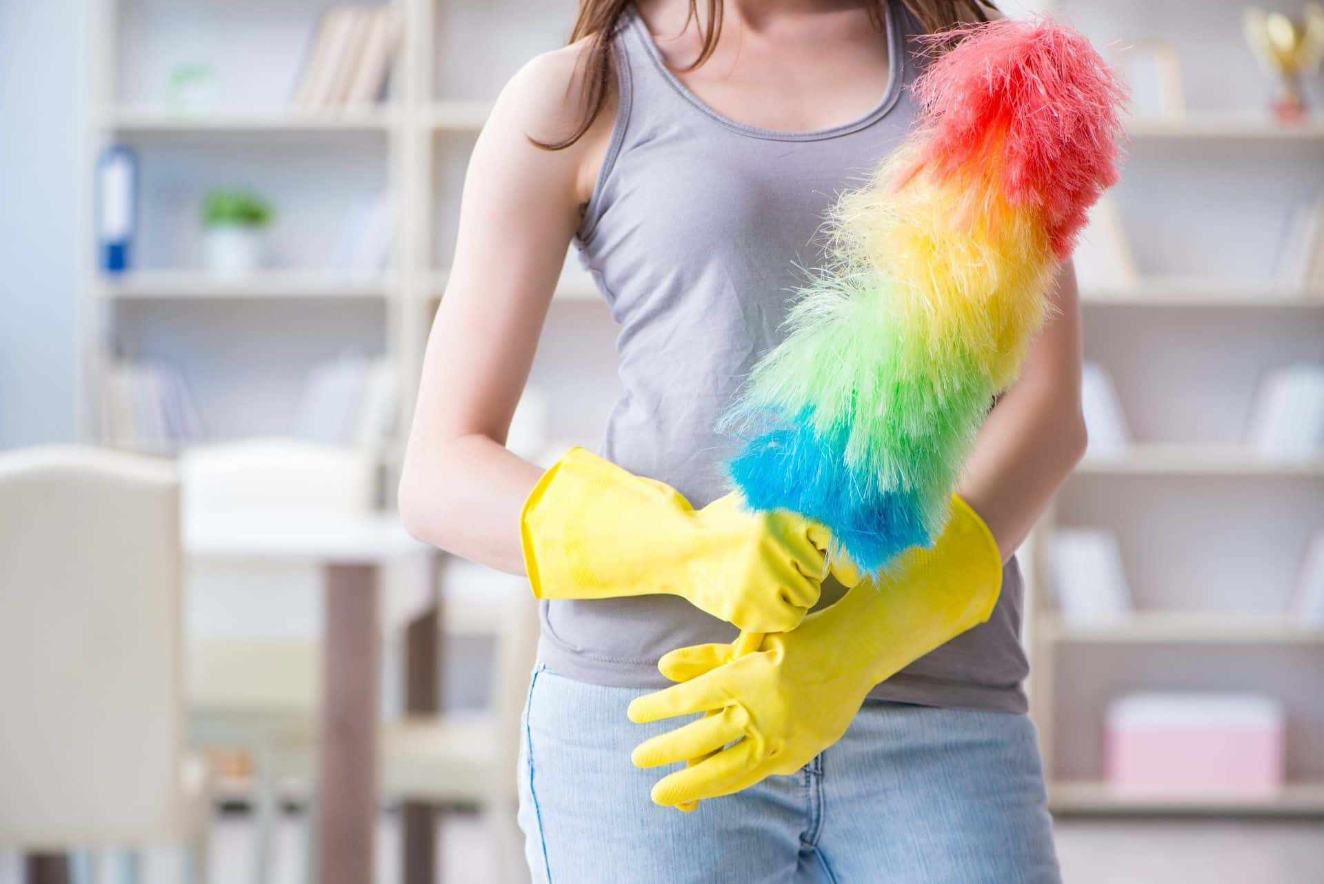 How Often You Should Really Be Dusting Your Home 1 woman in yellow rubber gloves holding a rainbow-colored duster