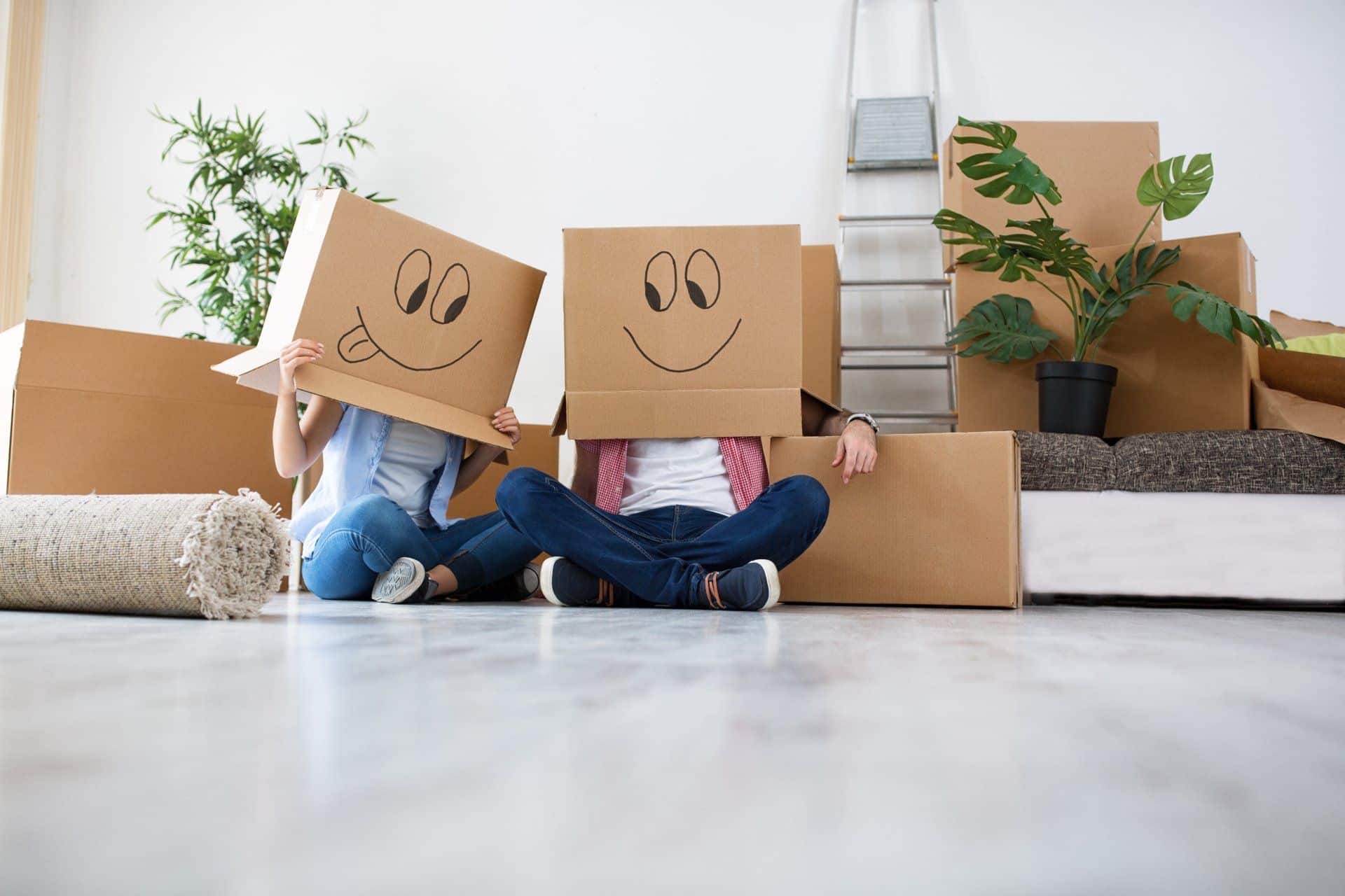 couple moving with cardboard boxes with happy faces drawn on them on their heads