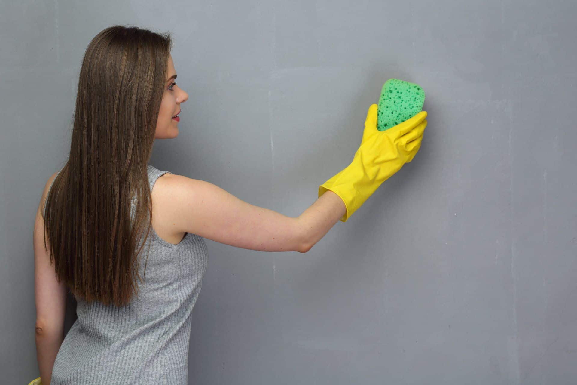 7 Cleaning Resolutions to Start Your New Year Off Right 6 woman using a sponge to clean a gray wall