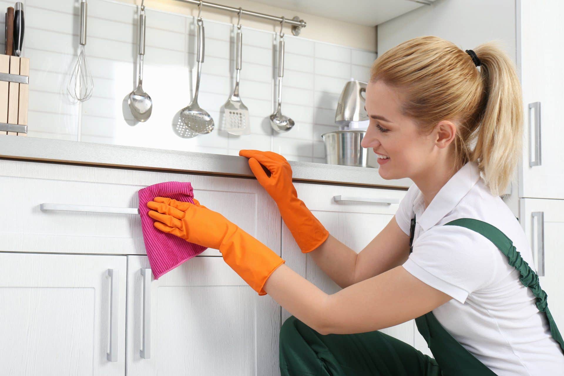 woman in orange cleaning gloves cleaning white cabinets
