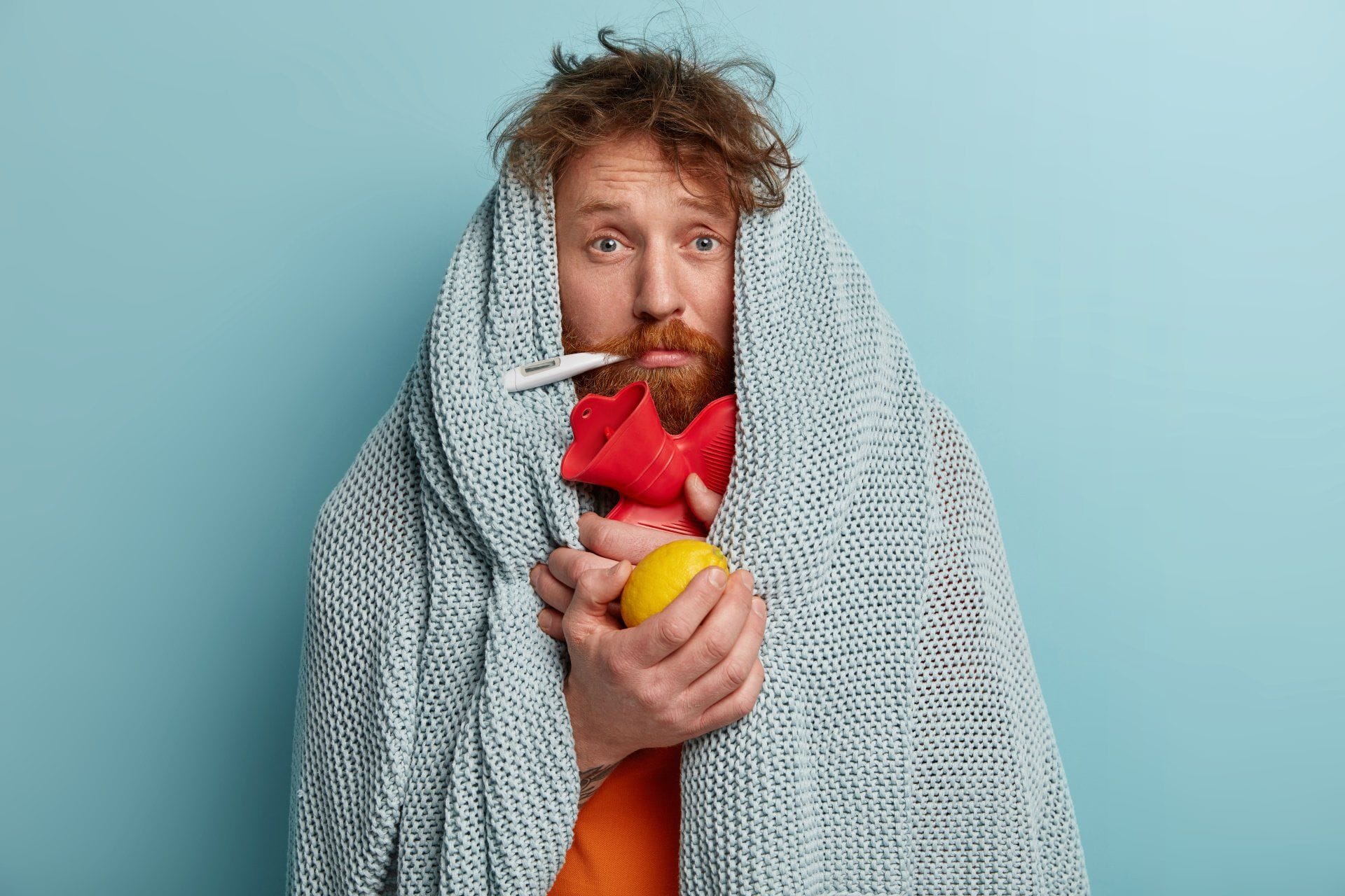a man wrapped in a blanket with a thermometer in his mouth because he is sick