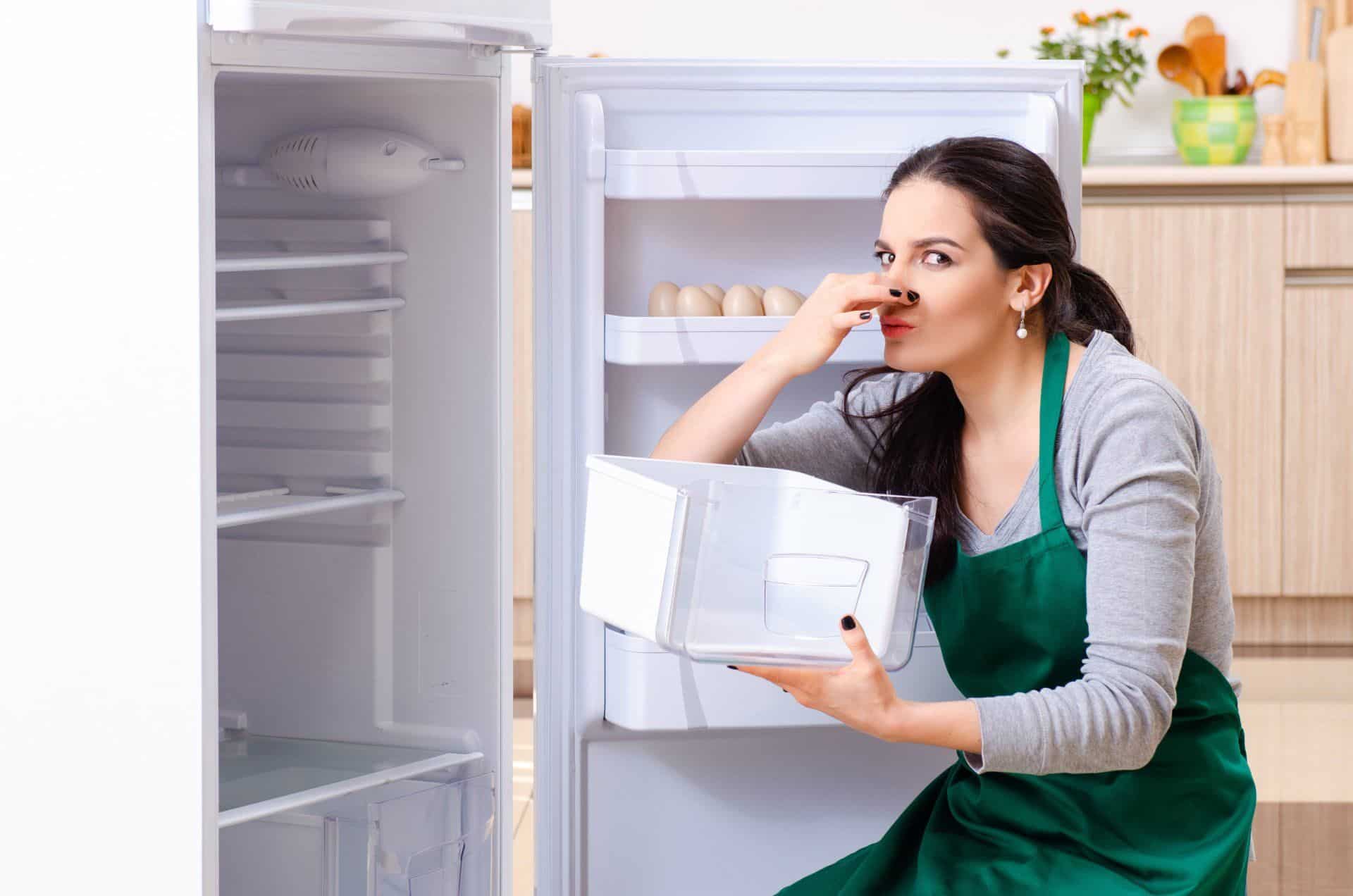 woman holding up fridge drawer plugging nose