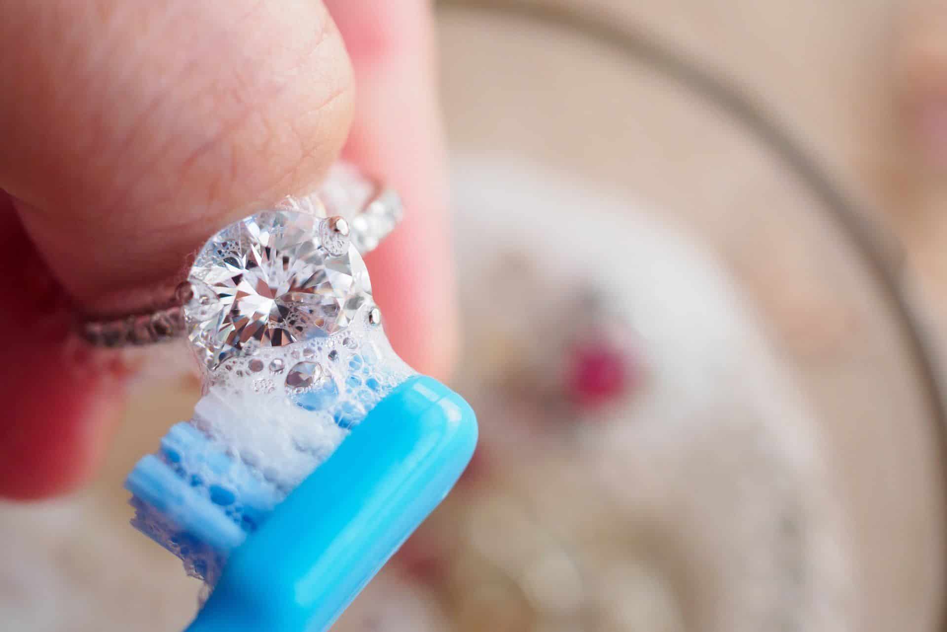 someone cleaning an engagement ring with a toothbrush and baking soda