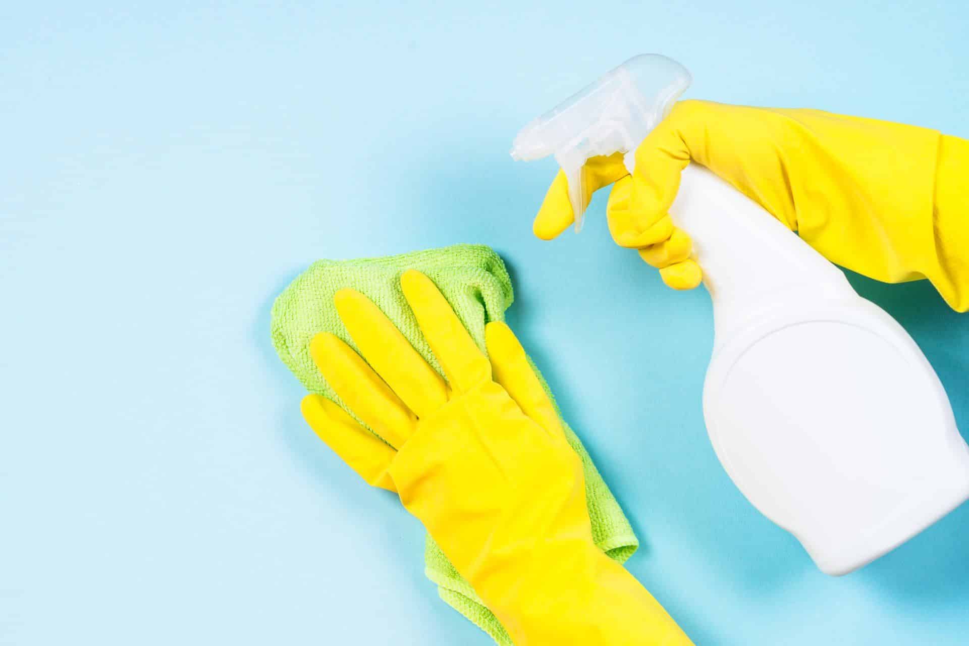 someone wearing yellow rubber gloves and cleaning with spray and microfiber cloth