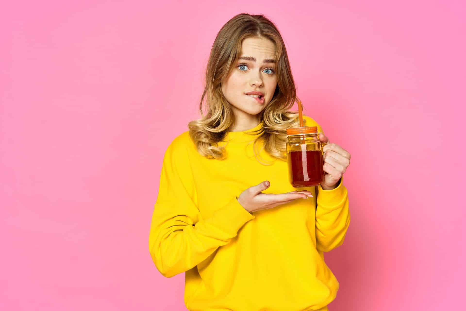 a woman on a pink background drinking iced tea