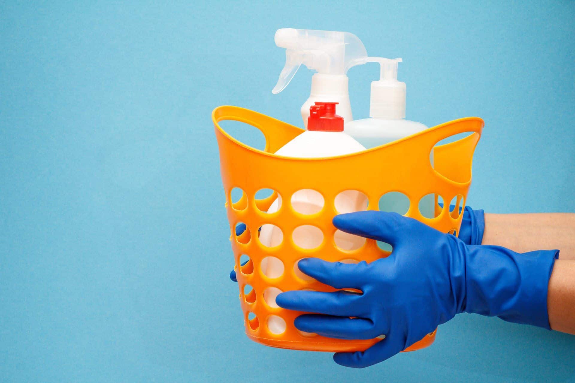 person in blue gloves holding a basket of cleaning supplies