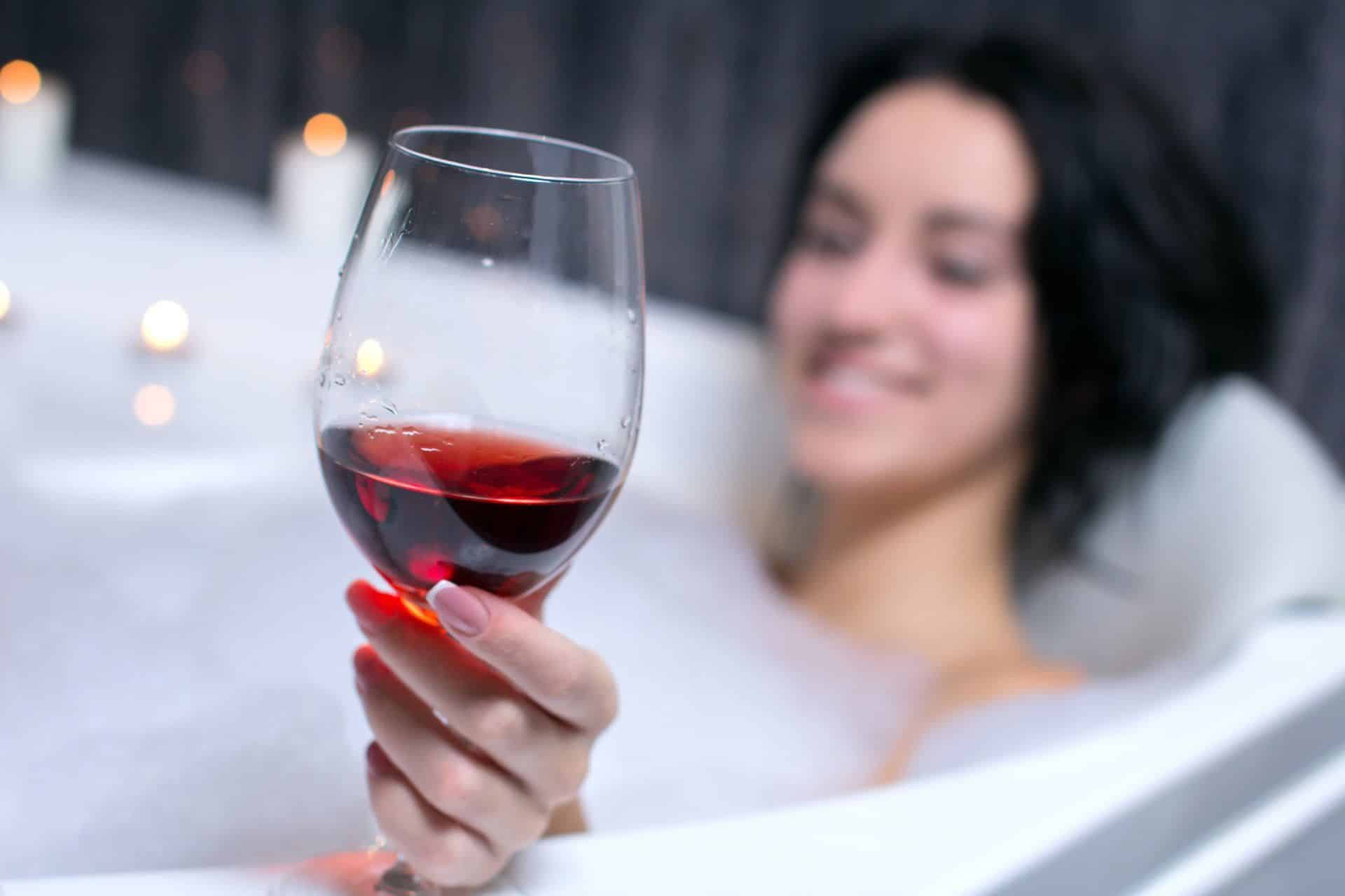 A woman enjoying a glass of red wine in a bath after learning about the best way to clean a bathtub.
