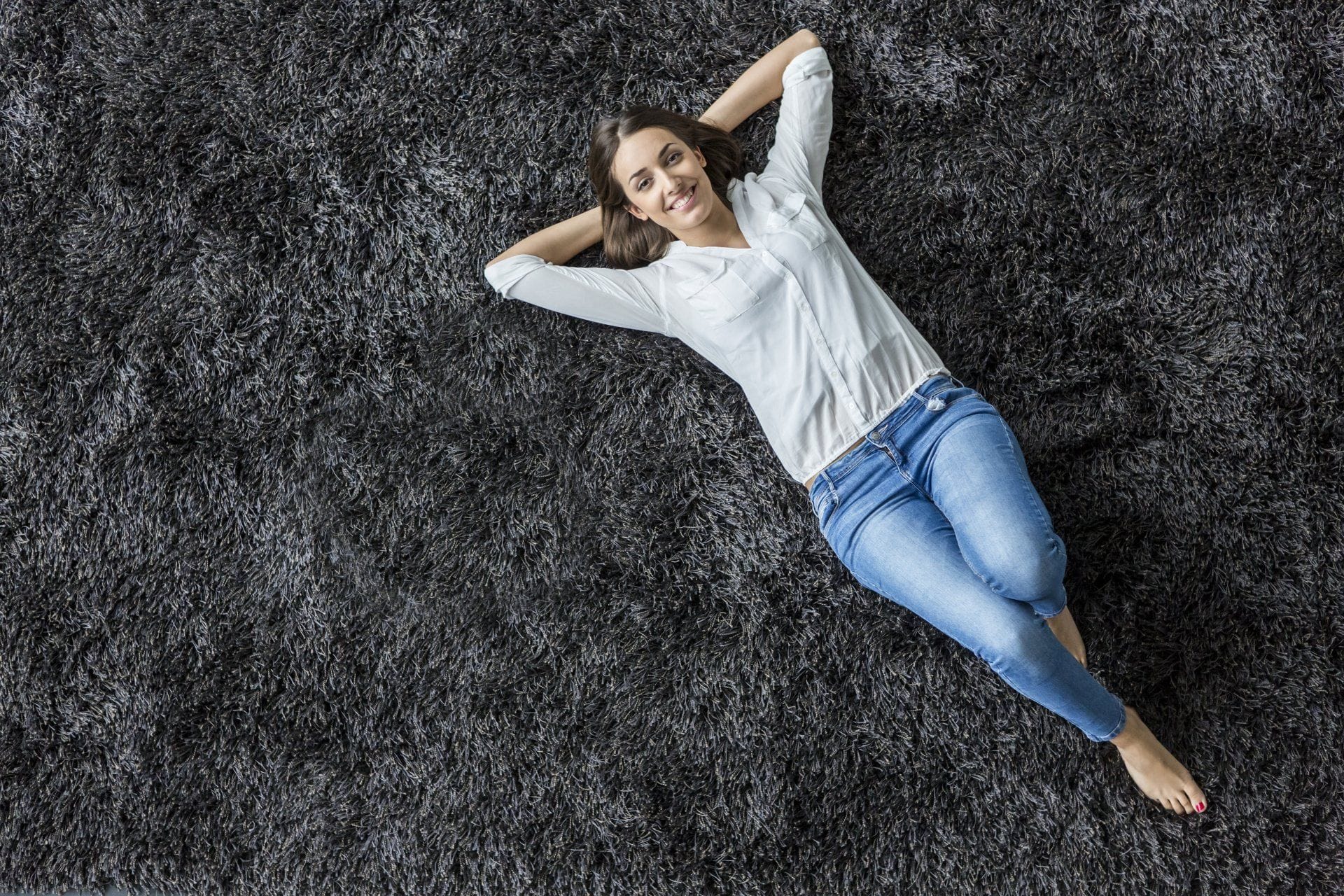smiling woman laying on a dark gray shag rug