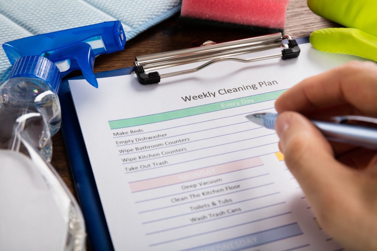 A person creating a weekly cleaning schedule for their home on a clipboard.