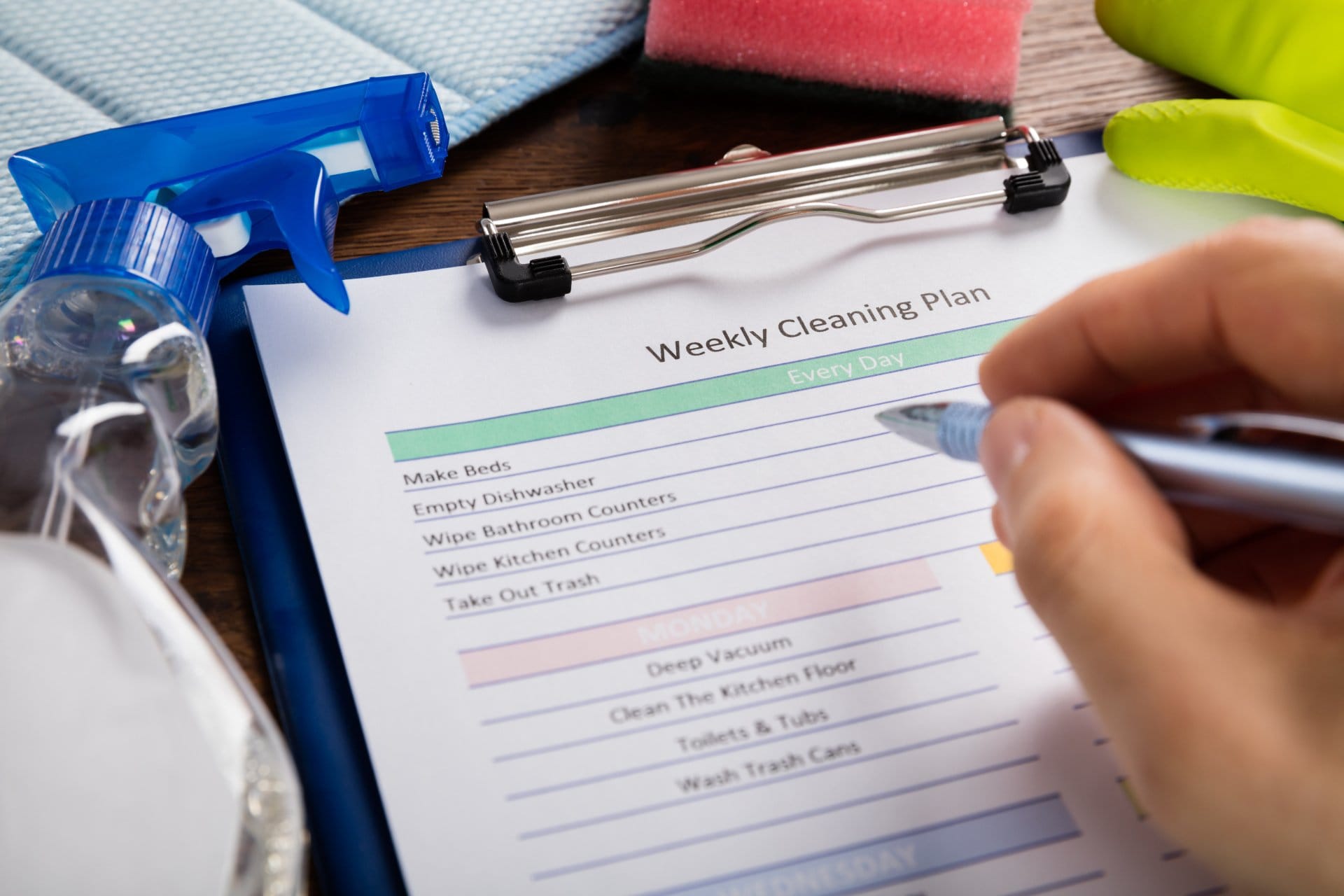 A person creating a weekly cleaning schedule for their home on a clipboard.