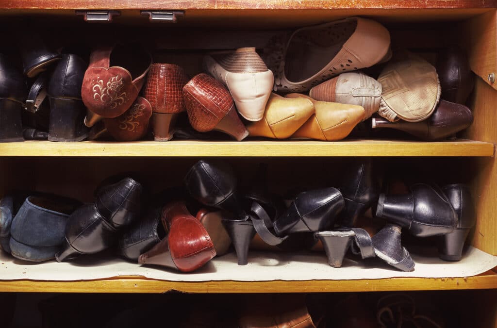 Cluttered shoes on shelves in a hall closet. View these tips for the best hall closet organization.