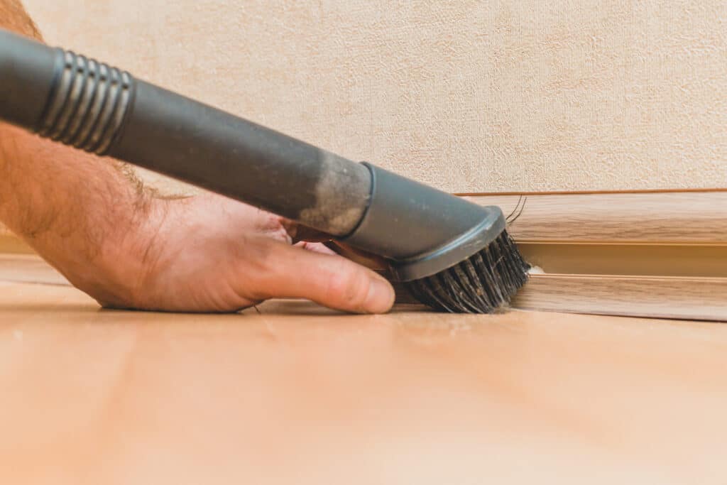 A man cleaning baseboards with a vacuum attachment