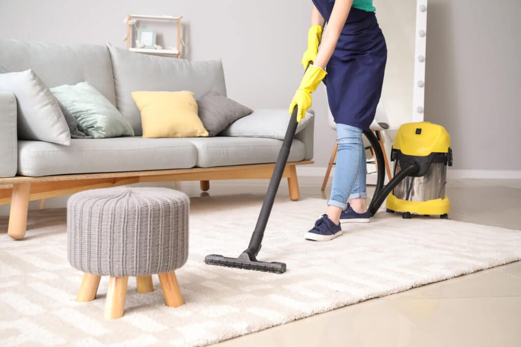 A professional cleaner using a yellow vacuum to clean an area rug