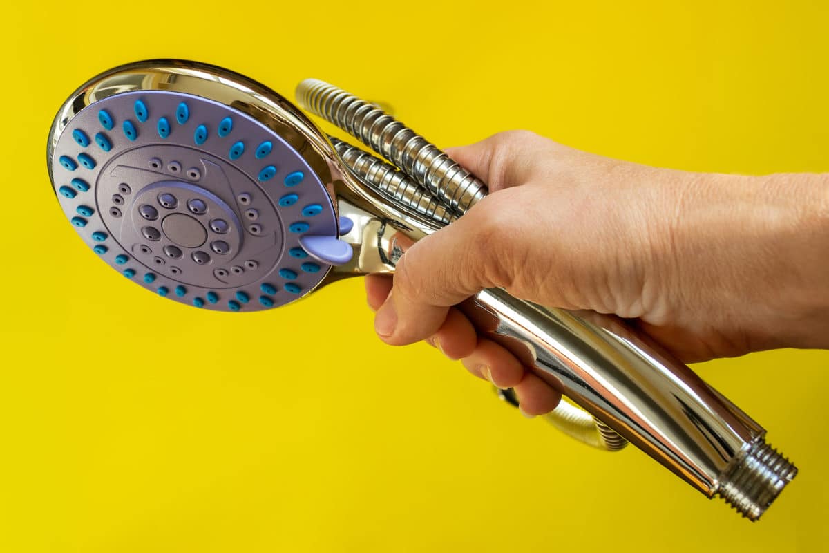 A person holding a showerhead on a yellow background