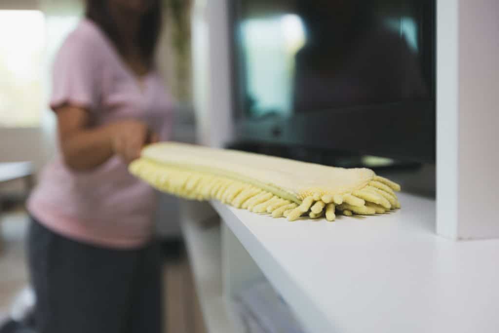 A woman dusting with a yellow microfiber duster.