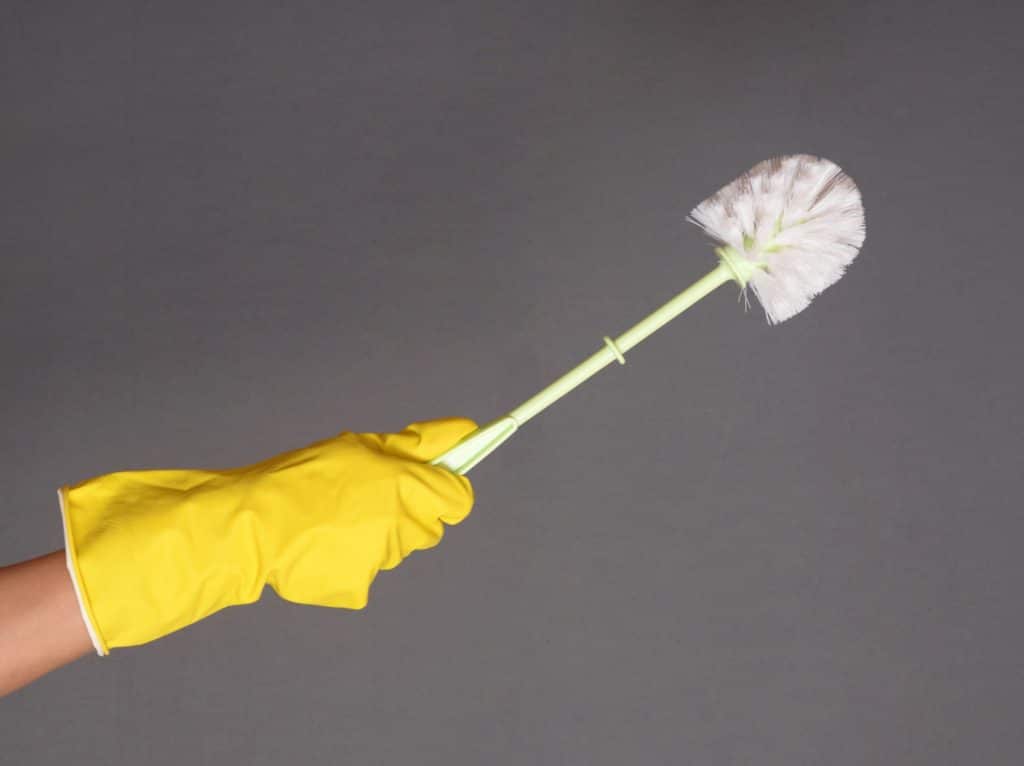 Someone wearing a yellow rubber glove and holding a toilet brush.
