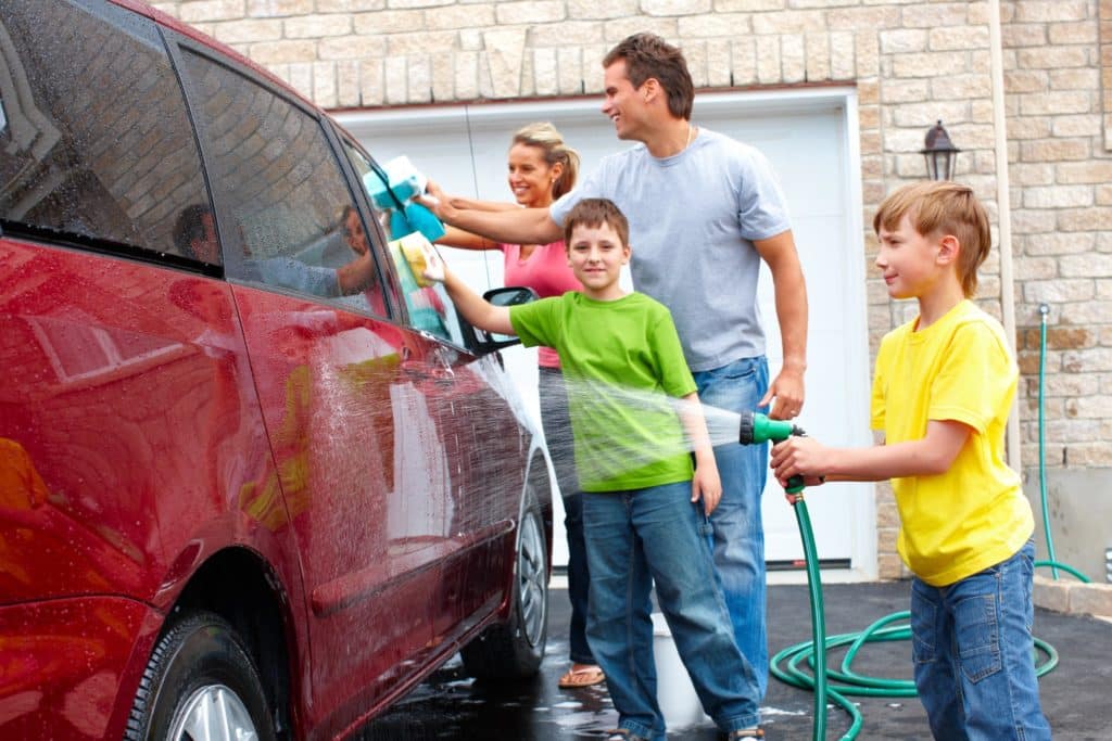A family of four washing their red van.