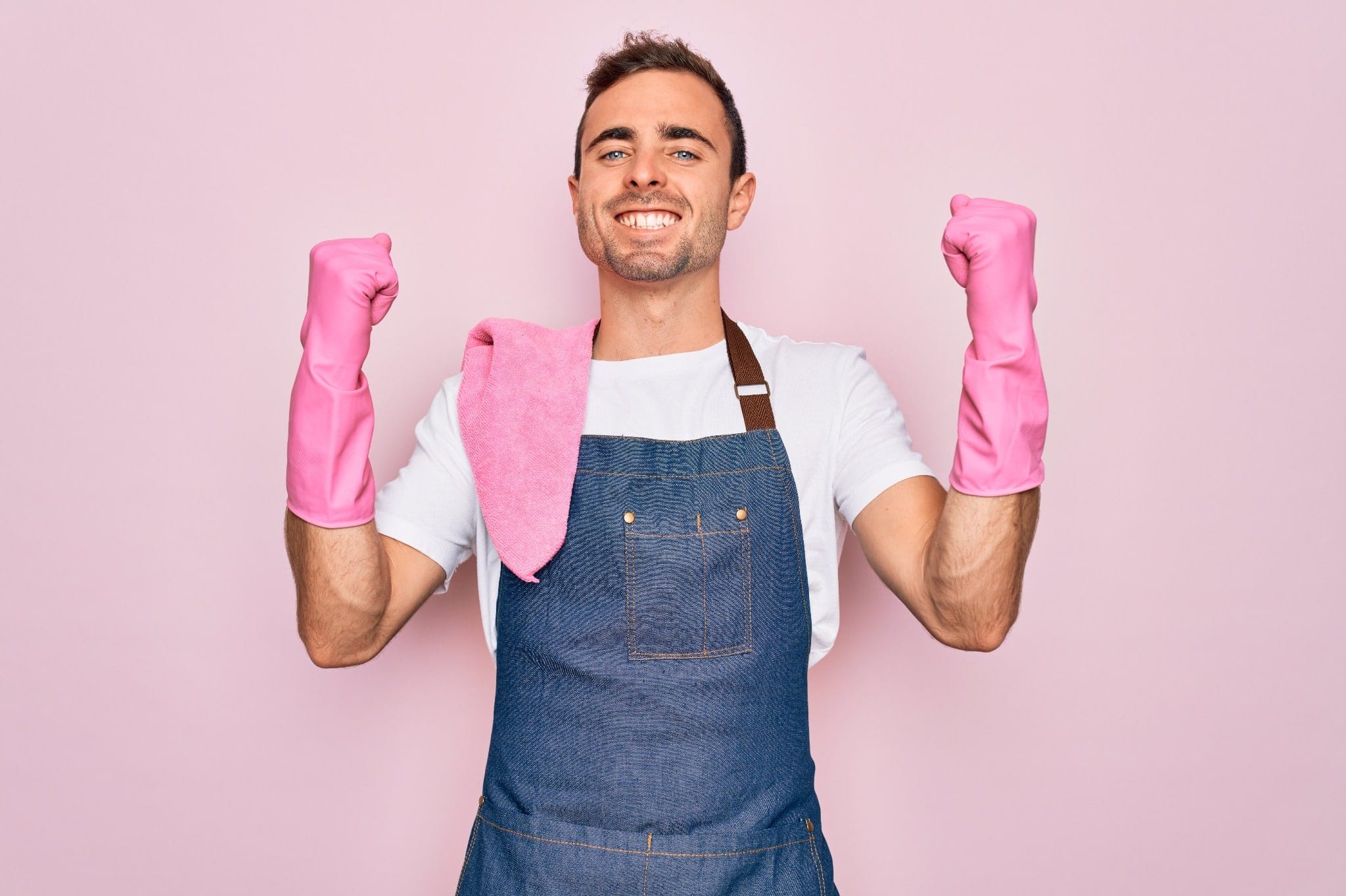 A man wearing an apron and pink cleaning gloves flexing and smiling for a portrait.