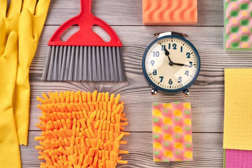13 Things to Try and Make Cleaning Fun 2 A flat lay of cleaning supplies and an alarm clock. Setting a timer is something your can try to make cleaning fun.
