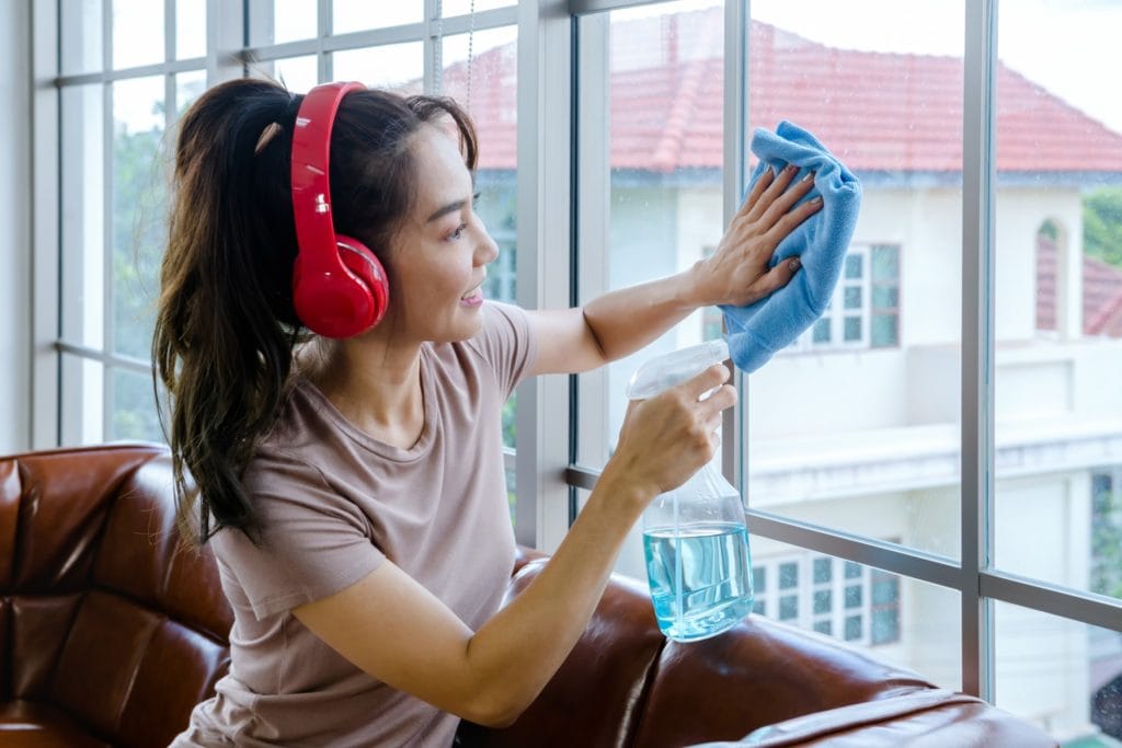 13 Things to Try and Make Cleaning Fun 9 A woman cleaning her windows while listening to a podcast using bright red headphones.