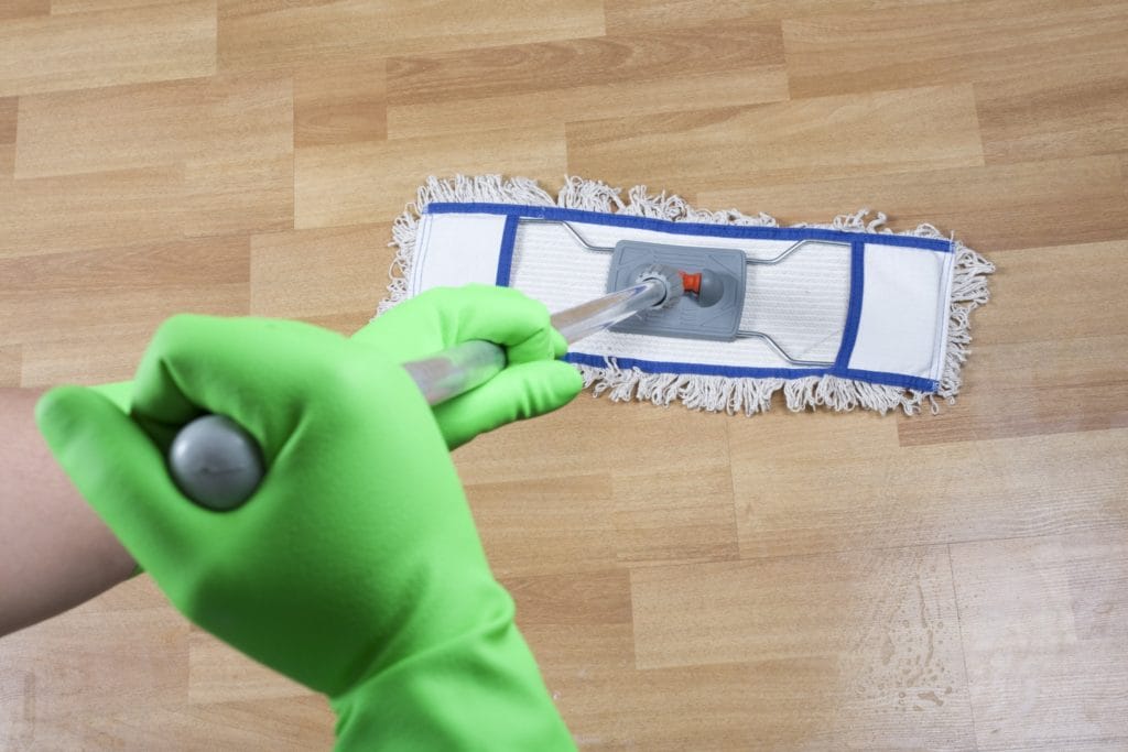A professional cleaner wearing bright green cleaning gloves mopping a hardwood floor.