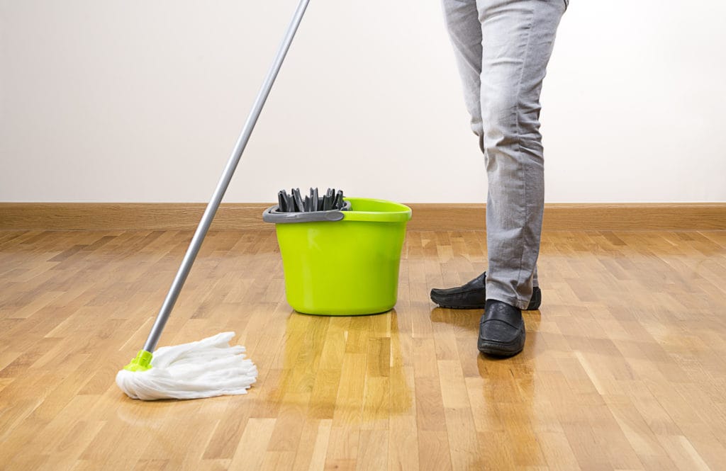 Someone wet mopping with a lime green bucket and mop. Mopping is the second step for how to clean hardwood floors.