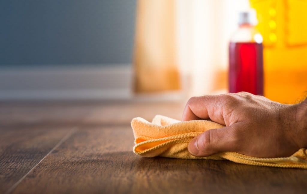 A man hand applying wood care products and cleaners on hardwood floor surface.