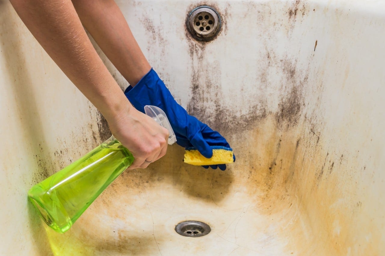Cleaning a Porcelain Tub: A Helpful TLC Cleaning Guide 2 Cleaning dirty old bathtub with corrosion and mould with detersive. Hands in blue rubber worker hand gloves hold sponge and spray with detergent clean bath tub covered in fungus, dirt and mold