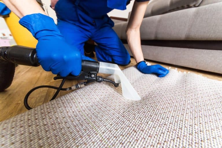 Cleaning service. Man janitor in gloves and uniform vacuum clean white carpet with professional equipment