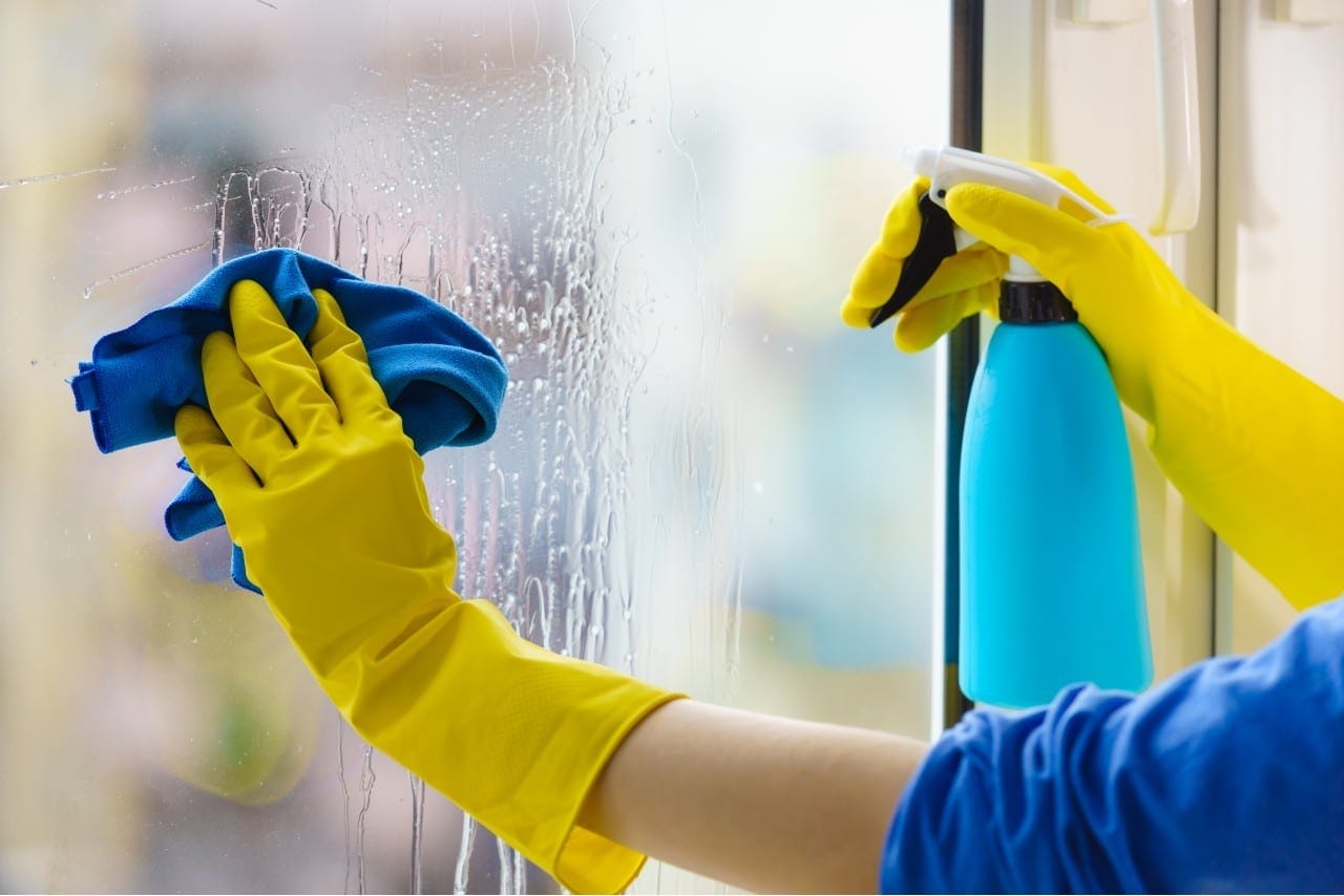 Gloved hand cleaning window rag and spray using glass cleaning products