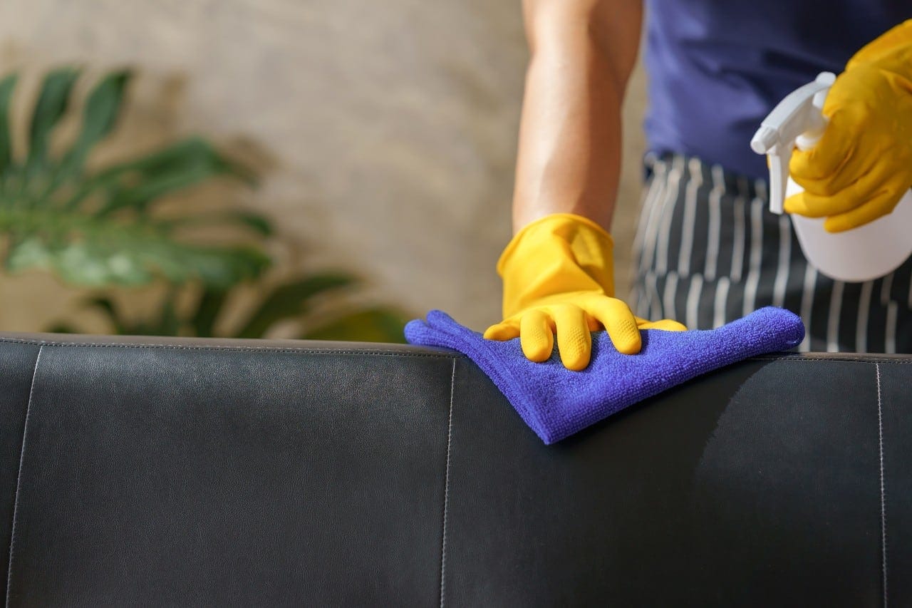 man cleaning leather sofas at home using furniture polish