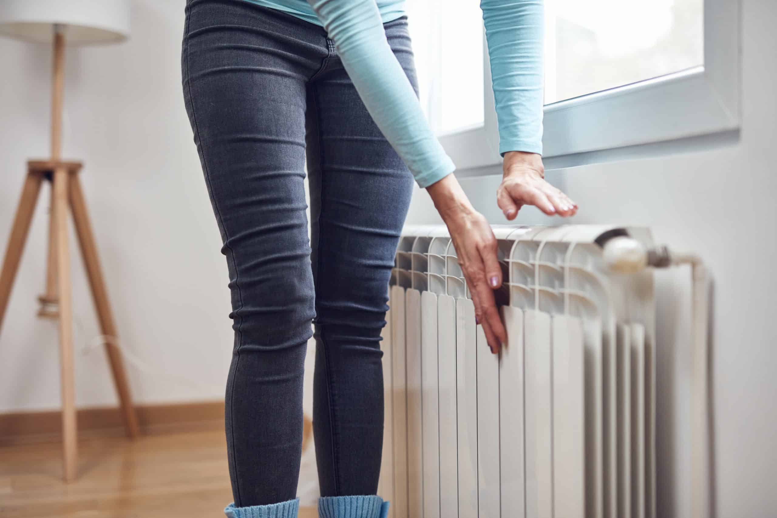 Woman heating her hands on the radiator during cold winter days