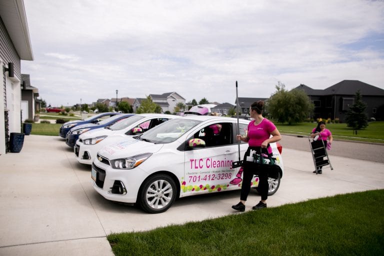 TLC Cleaning team members prepare for a new construction cleaning job, with branded vehicles and cleaning supplies ready in a residential neighborhood.
