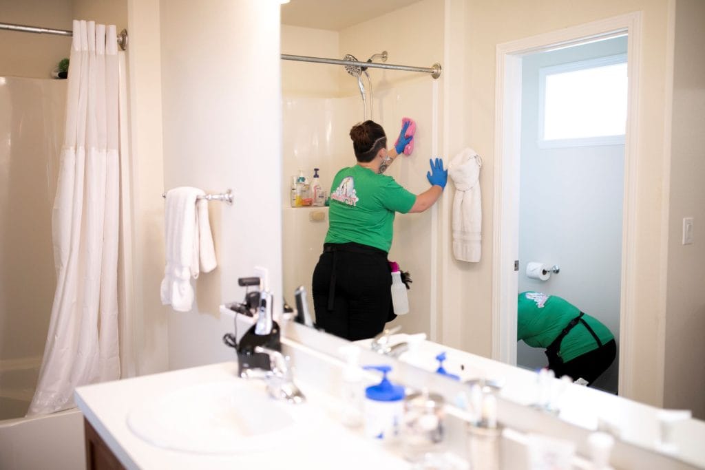 Two professional cleaners working in a bathroom, scrubbing the shower and toilet areas. Learn effective bathroom cleaning tips for maintaining a spotless space.